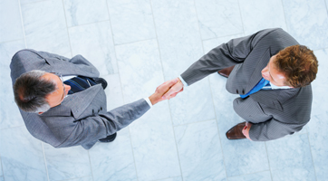 Looking down on two men in suites shaking hands with arms fully extended