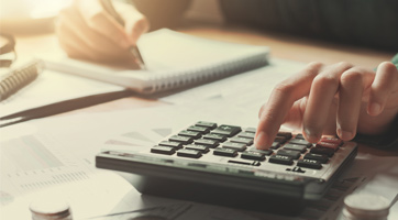 a person calculating on a calculator writing the results on a notebook