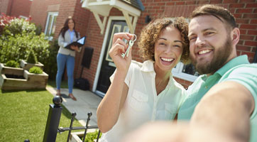 a selfie picture of a couple and their agent and house in the background