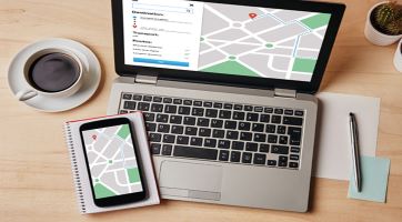 A laptop, smartphone, pad of paper with pen, and cup of coffee.