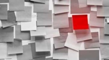 a black and white wall full of posted notes with one red one