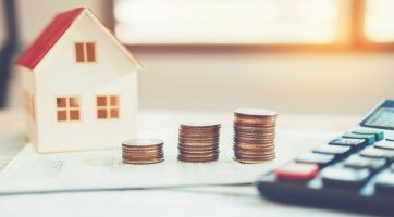 A tiny house next to three stacks of quarters.